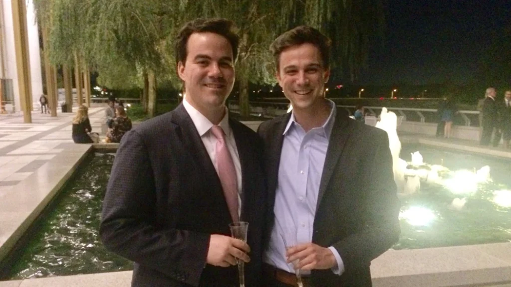 Two men in professional attire stand side-by-side outdoors at a networking event.