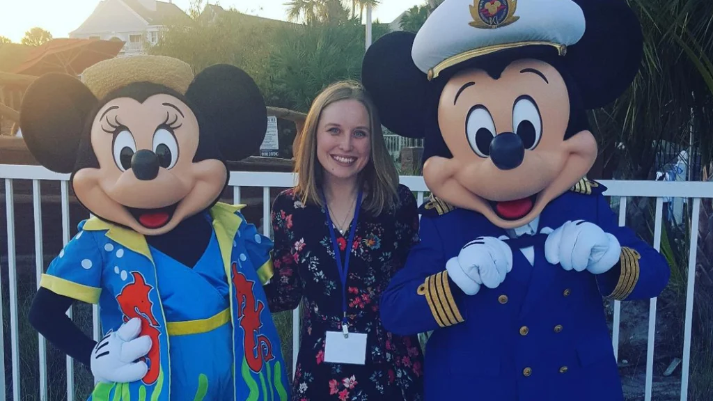 Mickey Mouse and Minnie Mouse stand with a woman in professional attire.