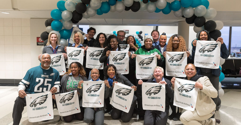 Group of people smiling while holding banners with the Eagles football logo under a balloon arch. Part of an American Airlines campaign by Ceisler Media & Issue Advocacy.