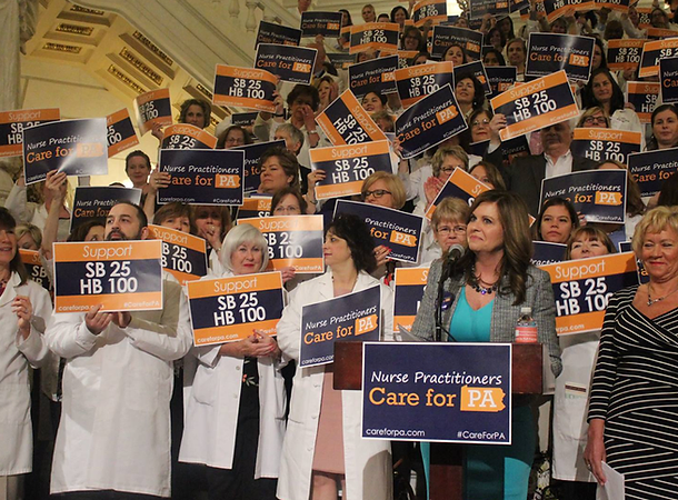 A large group gathers in the Pennsylvania Capitol Building with signs announcing that nurse practitioners care for PA, advocating for legislation changes.