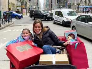 Ceisler Media's Kate Wilhelm sits in a carriage with her daughter wearing masks and carrying shopping bags with an American Girl doll sticking out