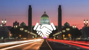 An icon of hands shaking in front of the Harrisburg Capitol building