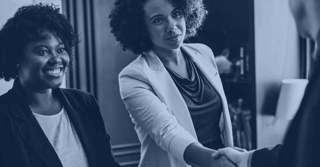 Two women in professional attire shake a person's hand