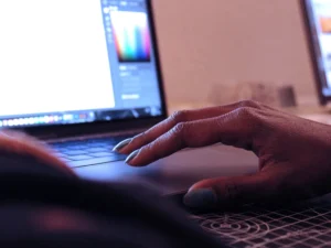 A woman's hand sits on a laptop while she works in an Adobe Suite platform