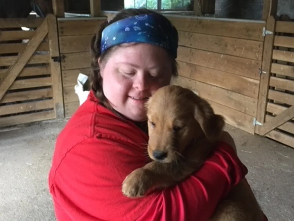 A woman holds a puppy in a barn