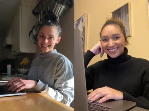 Interns Hannah and Maya work remotely, smiling from behind a laptop in their homes