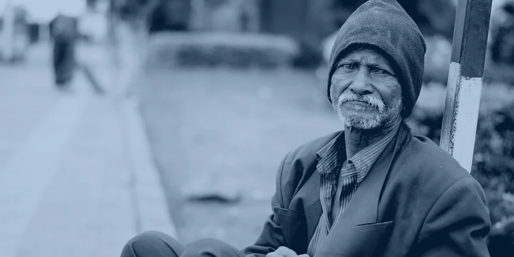 An elderly man in poverty sits on the ground