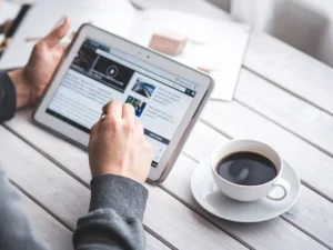 A person works on a tablet while drinking coffee out of a small cup