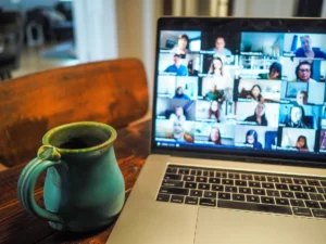 A laptop with many people in a virtual meeting while a cup of coffee sits on the table