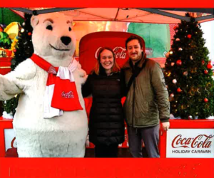 Makenna and Sam smiling and posing with a Coca-Cola polar bear mascot for the holidays.